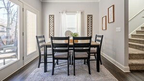 A dining area with a table and four chairs, a decorative wall panel, and a window with a view of trees. - Pet-Friendly 3BR Home Near I-85 and River Trails (Norcross)
