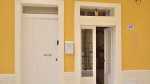En hotellentrédörr med en vit dörr, ett litet fönster ovanför dörren och en väggmonterad ljusströmbrytare.