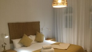 A neatly made bed with a brown headboard, white pillows, and a yellow blanket. There is a bedside table with a lamp and a small vase with dried flowers. - Cozy Villa by MAHBO (A) (Corralejo)