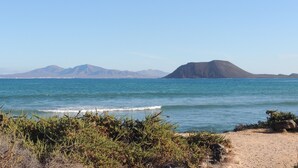 A coastal landscape with a clear sky, a sandy beach, and distant mountains. - Cozy Villa by MAHBO (A) (Corralejo)