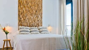 A bedroom with a bed, bedside lamps, a wall art piece, and a window with curtains. - Casa Grace (Nerja)