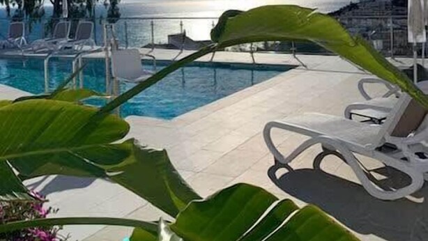 A poolside area with lounge chairs, a view of the sea, and tropical plants. - Casa Grace (Nerja)