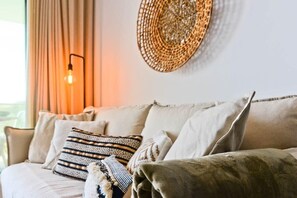 A beige sofa with patterned cushions, a woven wall decoration, and a wall-mounted light fixture.