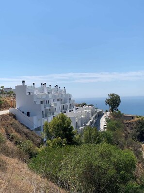 Um edifício moderno branco com várias varandas, localizado numa encosta com vista para o mar.