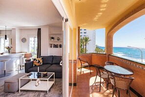A living room with a sofa, coffee table, and a balcony with a view of the ocean.