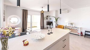 A modern kitchen with a central island, a dining area with a round table, and a living space with a sofa and a TV. - Toboso 1 (Nerja)