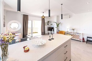 A modern kitchen with a central island, a dining area with a round table, and a living space with a sofa and a TV.
