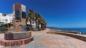 A plaza with a stone monument, palm trees, and a view of the sea. - Toboso 1 (Nerja)