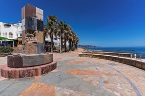 A plaza with a stone monument, palm trees, and a view of the sea.