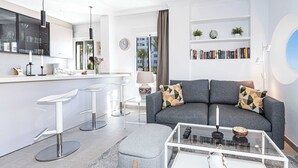 A modern living room with a grey sofa, a glass coffee table, and a kitchen area with white bar stools. - Toboso 1 (Nerja)