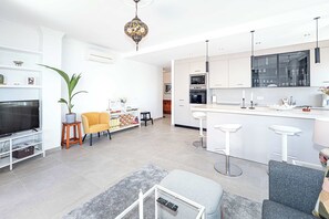 A modern kitchen with white cabinets, a central island with bar stools, a TV, and a potted plant. - Toboso 1 (Nerja)