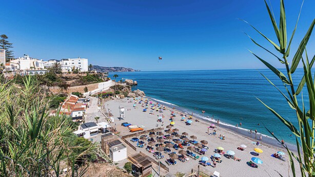 A beach with umbrellas, people, and buildings in the background. - Toboso 1 (Nerja)
