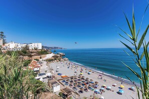 A beach with umbrellas, people, and buildings in the background. - Toboso 1 (Nerja)
