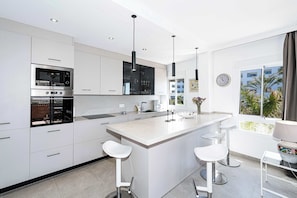 A modern kitchen with white cabinetry, stainless steel appliances, and a large island with bar stools. - Toboso 1 (Nerja)
