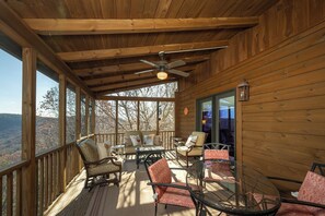 A wooden deck with outdoor furniture, a ceiling fan, and a view of the surrounding landscape.