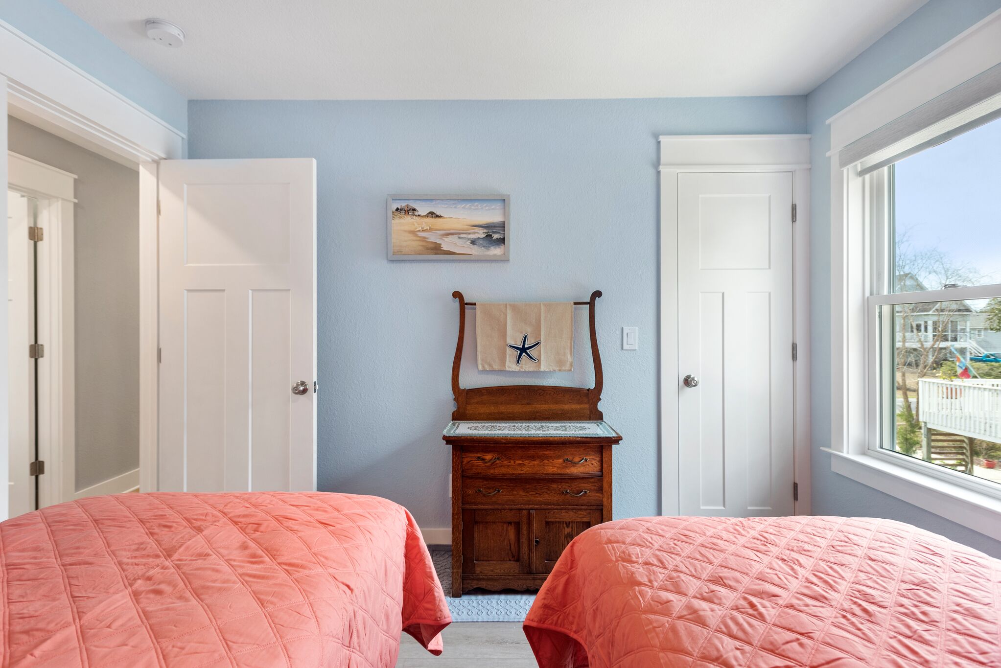 Quarto com duas camas, cômoda, um quadro e janela com vista.