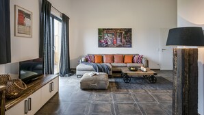 Una sala moderna con un sofá, reposapiés y televisor sobre un mueble de madera.