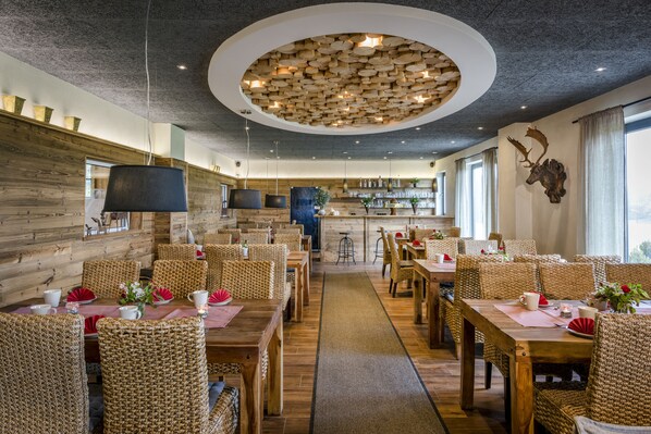 Ein Restaurant mit Holzwänden, Korbmöbeln und einem zentralen Deckenornament.