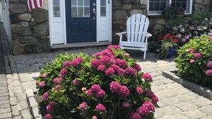 A stone house with a dark blue door, an American flag, a white chair, and pink hydrangea bushes. - Brigantine Cottage - Experience both an Ocean AND Bay Family Vacation  this year (Brigantine)
