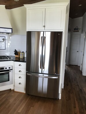 A stainless steel refrigerator in a kitchen with white cabinetry and a wooden floor.