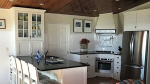 A kitchen with a central island, white cabinetry, a stainless steel refrigerator, and a dining area with white chairs. - Brigantine Cottage - Experience both an Ocean AND Bay Family Vacation  this year (Brigantine)