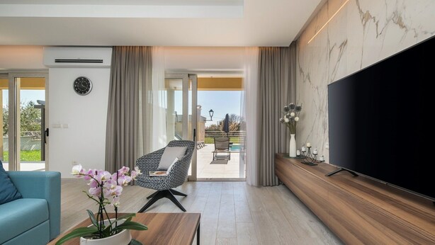 A modern living room with a flat-screen TV, a sofa, a coffee table with a plant, and a balcony with outdoor seating.