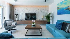 A modern living room with a large TV, a coffee table, a sofa, and a painting on the wall.