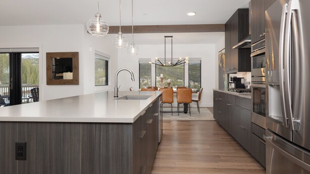 A modern kitchen with a large island, stainless steel appliances, and a dining area with a view. - Beaverhead Village Haven | Hot Tub • Walk to Big Sky (Big Sky)