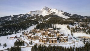 A ski resort with multiple buildings, a mountain in the background, and snow-covered terrain. - Beaverhead Village Haven | Hot Tub • Walk to Big Sky (Big Sky)