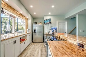 A modern kitchen with a wooden countertop, stainless steel appliances, and a large window overlooking a patio area.
