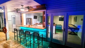 A bar area with a counter and stools, a ceiling fan, and a sliding glass door leading to a living space.