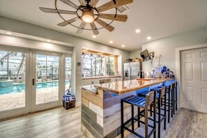 A modern kitchen with a central island, bar stools, a ceiling fan, and a view of a pool outside.