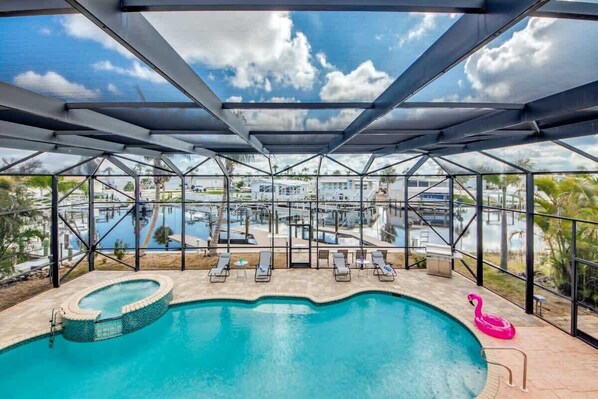 A swimming pool with lounge chairs and a pink flamingo float, surrounded by a glass enclosure with a view of a marina.