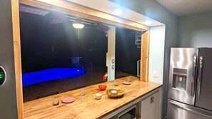 A kitchen with a wooden countertop, a stainless steel refrigerator, and a view of a swimming pool.