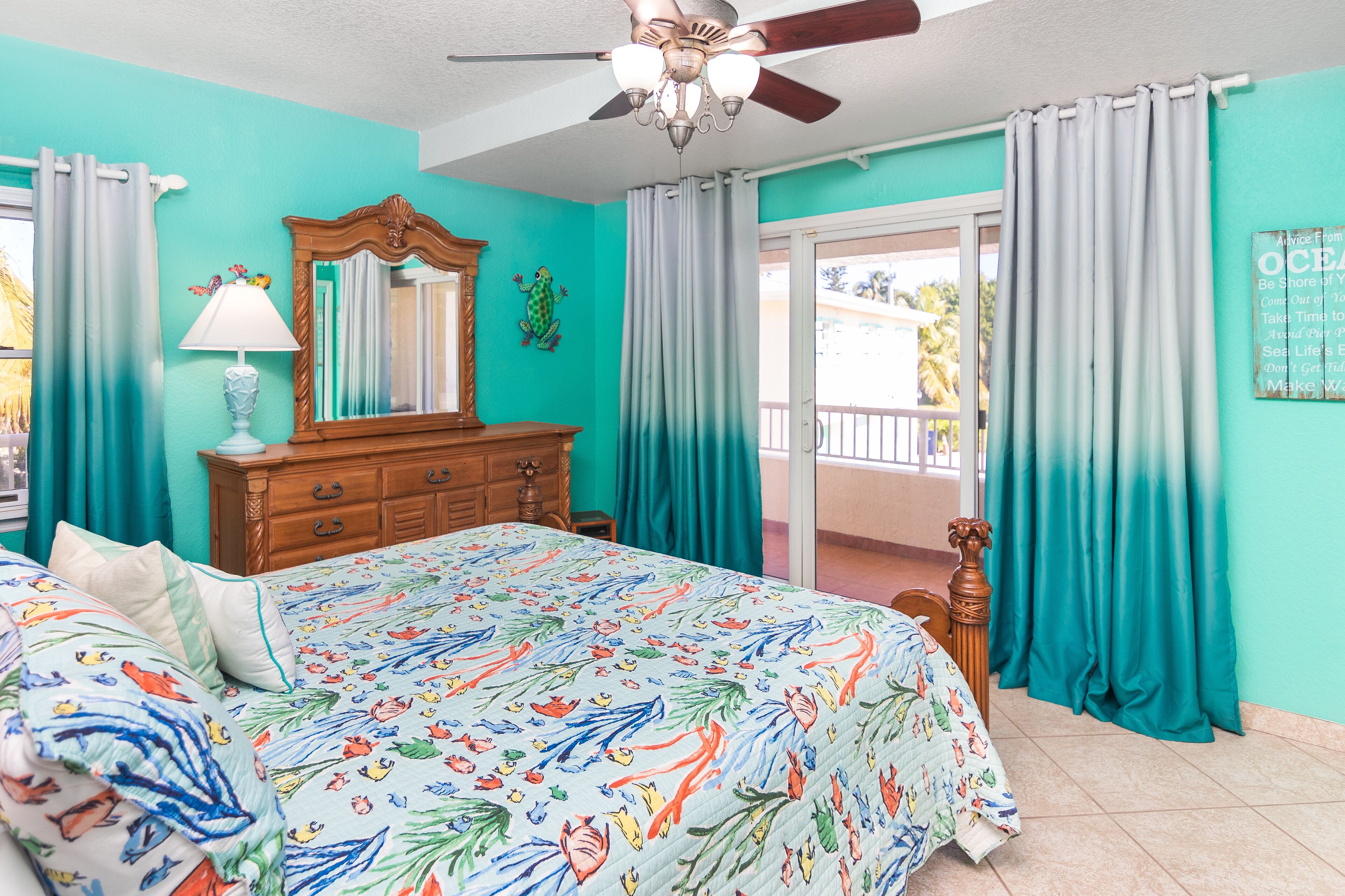 A bedroom with a bed, a ceiling fan, a dresser, and a view of the outside.