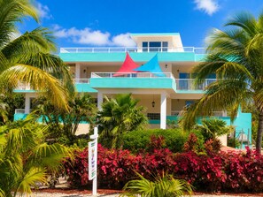 A multi-story hotel with a blue and white facade, a red and blue roof, and surrounded by tropical vegetation.