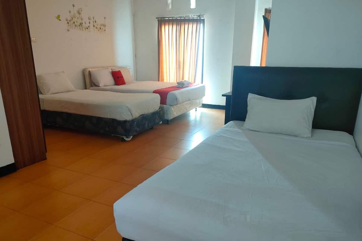 Ein Hotelzimmer mit einem großen Bett, zwei kleineren Betten, Holzboden und einem Fenster mit Vorhängen.