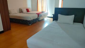 A hotel room with a large bed, two smaller beds, a wooden floor, and a window with curtains.