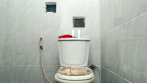 A bathroom with a toilet, a red pillow on the seat, and a shower hose. - Cozy Residence Cipedes Bandung (Bandung)