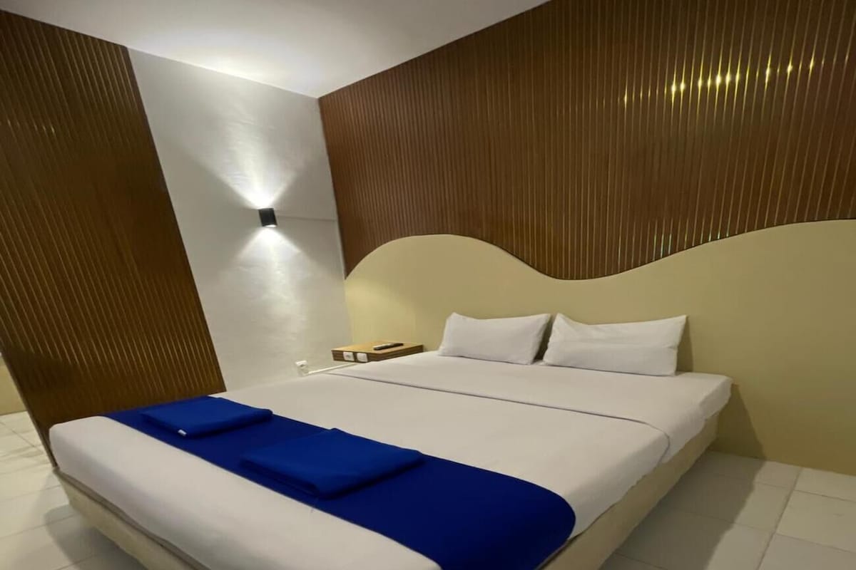 Ein modernes Hotelzimmer mit einem großen Bett, einem Nachttisch und einer wandmontierten Lampe.