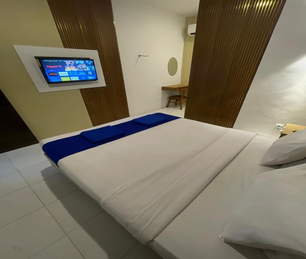 A hotel room with a bed, a TV mounted on the wall, and a desk with a chair.