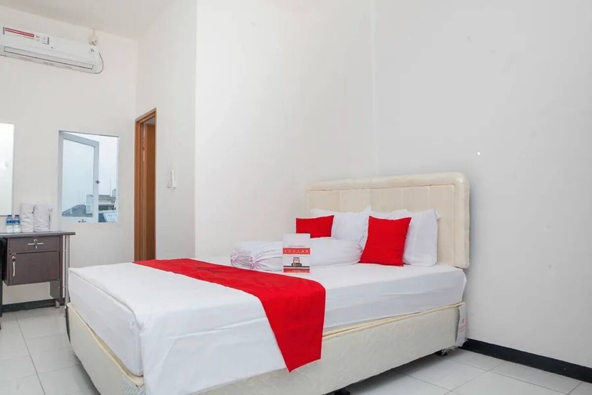 Ein Hotelzimmer mit einem Bett, einem Nachttisch, einem Spiegel und einer Klimaanlage.