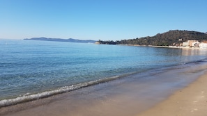 A beach with clear water, a sandy shore, and buildings in the background.