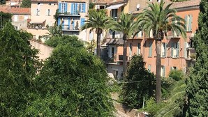 A hillside residential area with multi-story buildings, some with balconies, surrounded by lush greenery and palm trees.