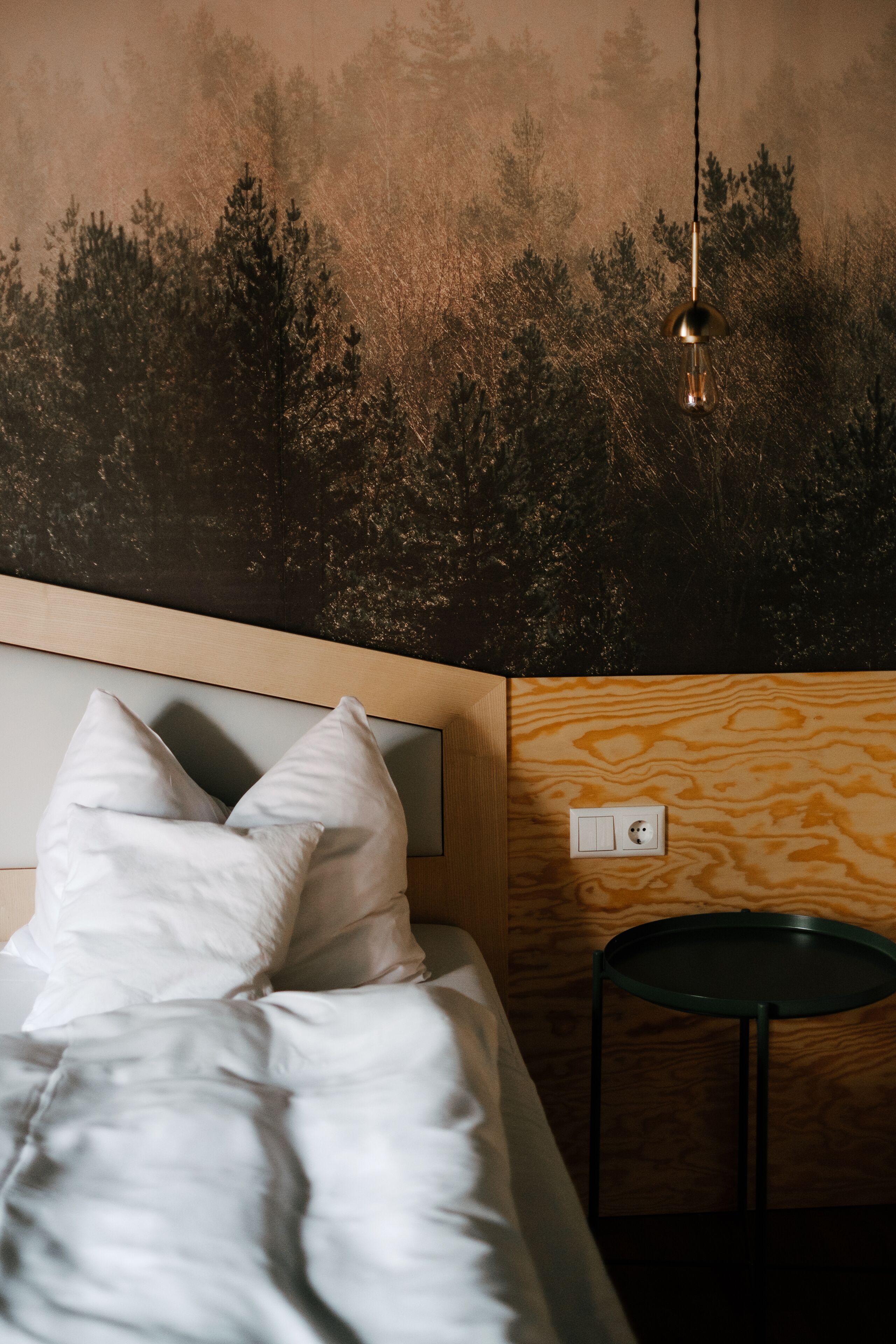 A bedroom with a bed, pillows, a wall-mounted light fixture, and a small table.