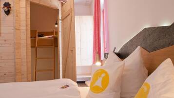 Un dormitorio con una cama litera de madera, una cama con ropa de cama blanca y un cabecero con panel gris.