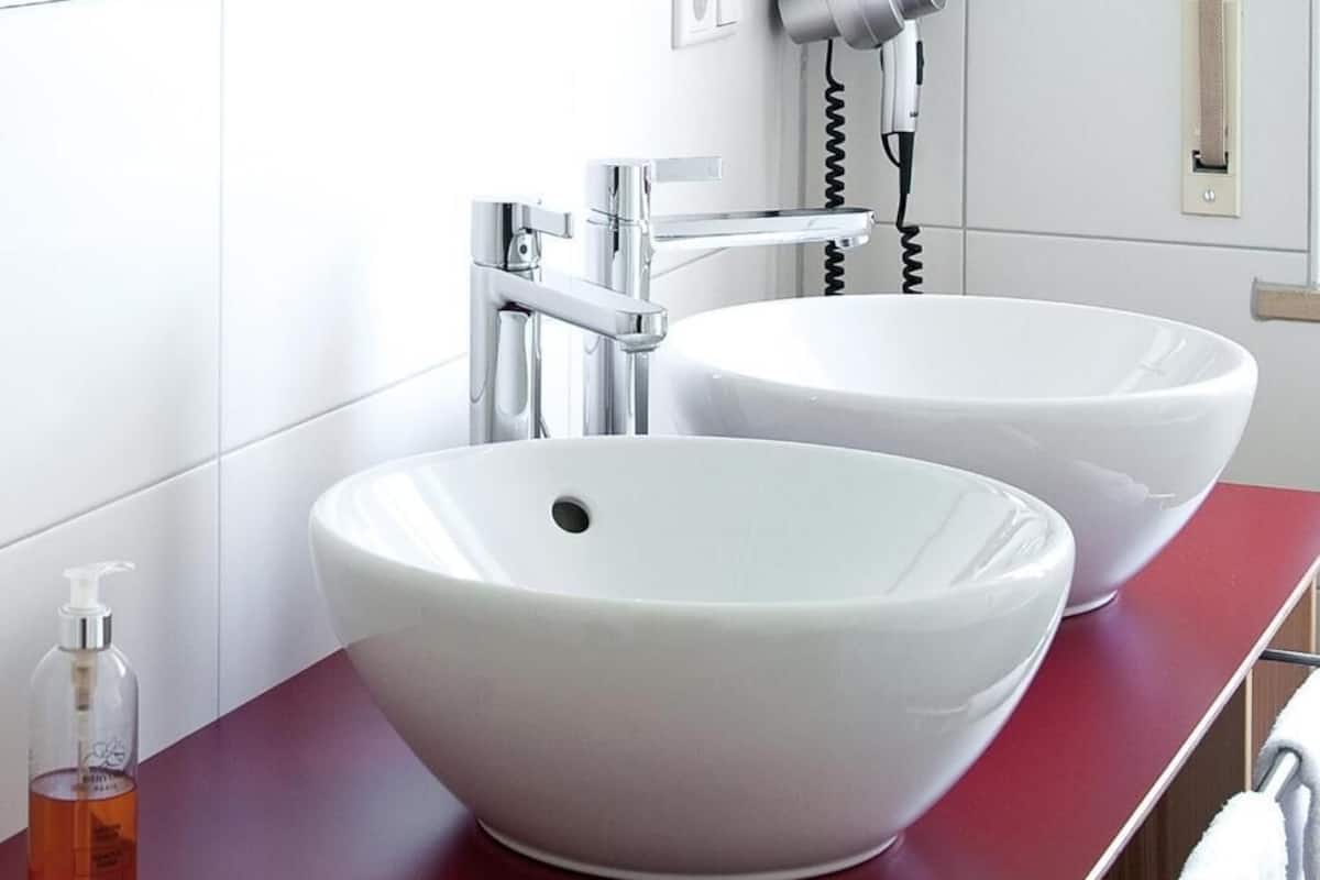 A bathroom with two white vessel sinks, a red countertop, and a hairdryer mounted on the wall.