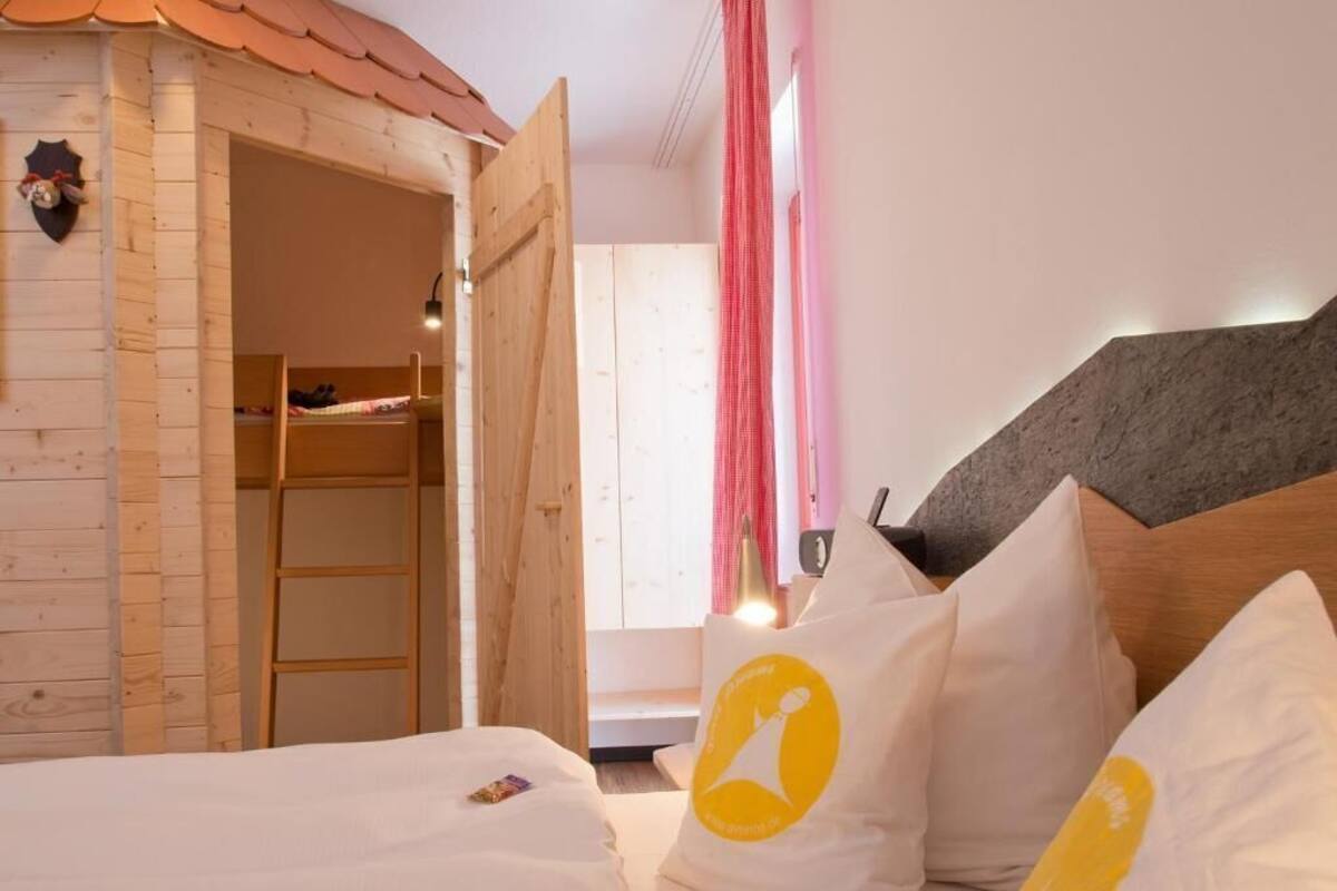 A bedroom with a wooden bunk bed, a bed with white bedding, and a headboard with a grey panel.