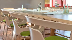 Un comedor con una mesa larga, varias sillas y un ventanal con cortinas rojas.