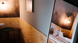 Habitación de hotel moderna con una pared de acento de madera, una obra de arte enmarcada, una cama con ropa blanca y una lámpara colgante.